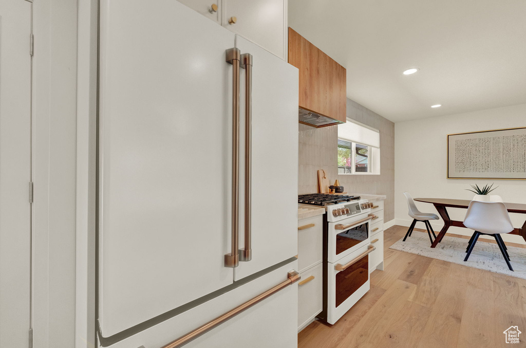Kitchen with white appliances, tasteful backsplash, light wood-type flooring, and white cabinetry