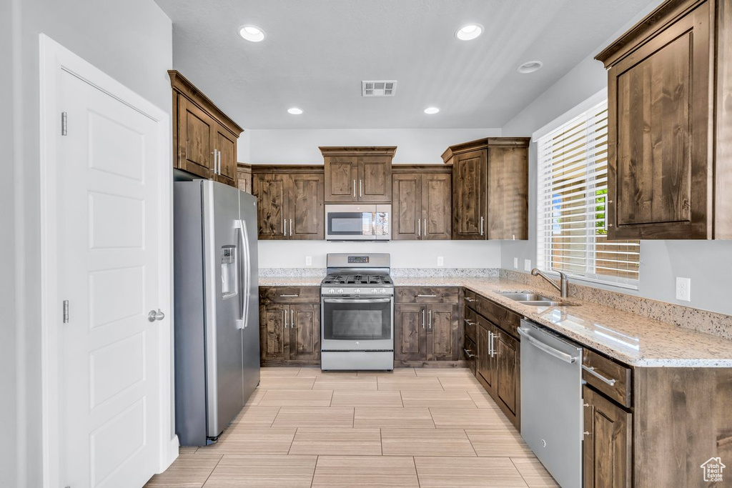 Kitchen featuring light stone counters, stainless steel appliances, light tile floors, sink, and dark brown cabinetry
