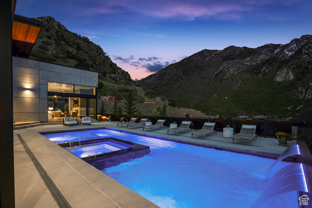 Pool at dusk with pool water feature, a mountain view, an in ground hot tub, and a patio