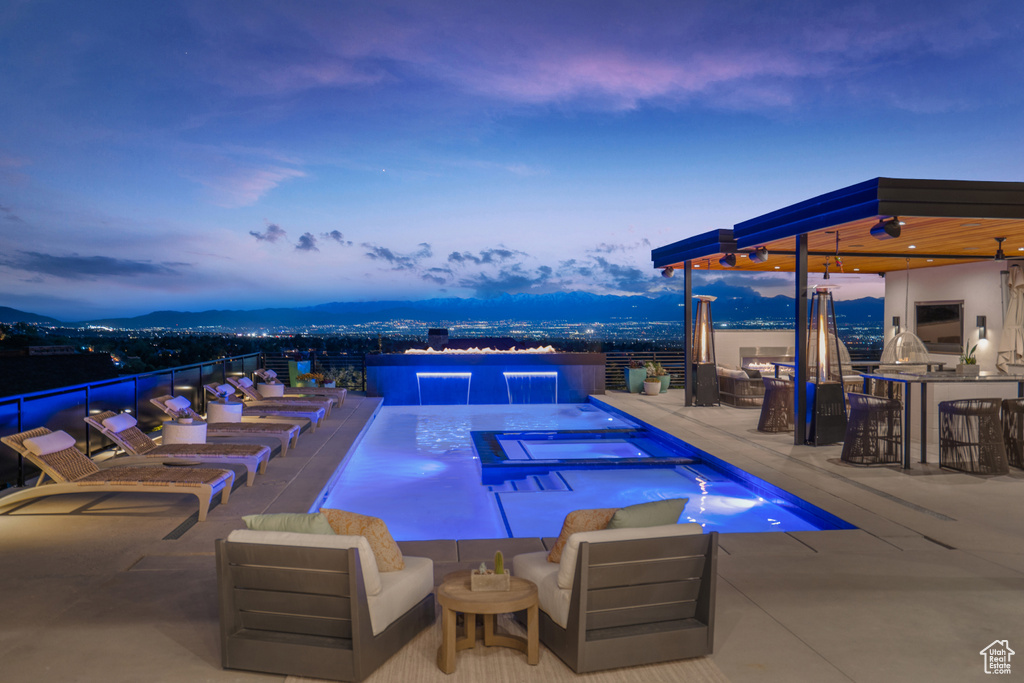 Pool at dusk with a patio area, a mountain view, exterior bar, and an outdoor hangout area