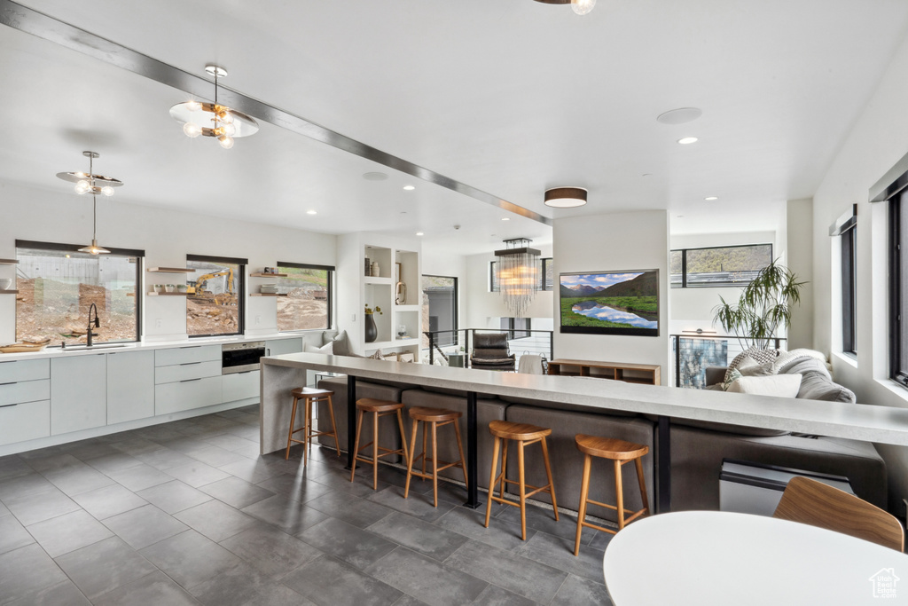 Kitchen featuring decorative light fixtures, a breakfast bar, white cabinets, sink, and dark tile flooring