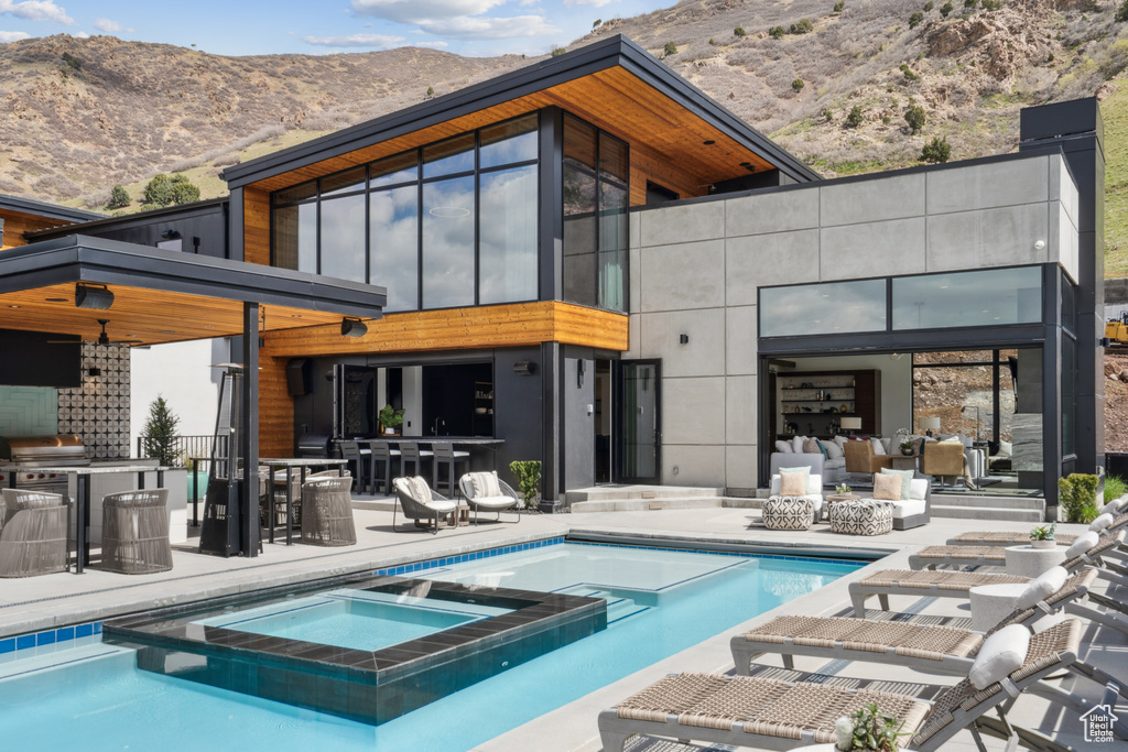 Rear view of property featuring a mountain view, exterior bar, a patio, and a pool with hot tub