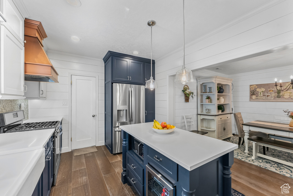 Kitchen featuring decorative light fixtures, dark wood-type flooring, appliances with stainless steel finishes, custom range hood, and blue cabinets