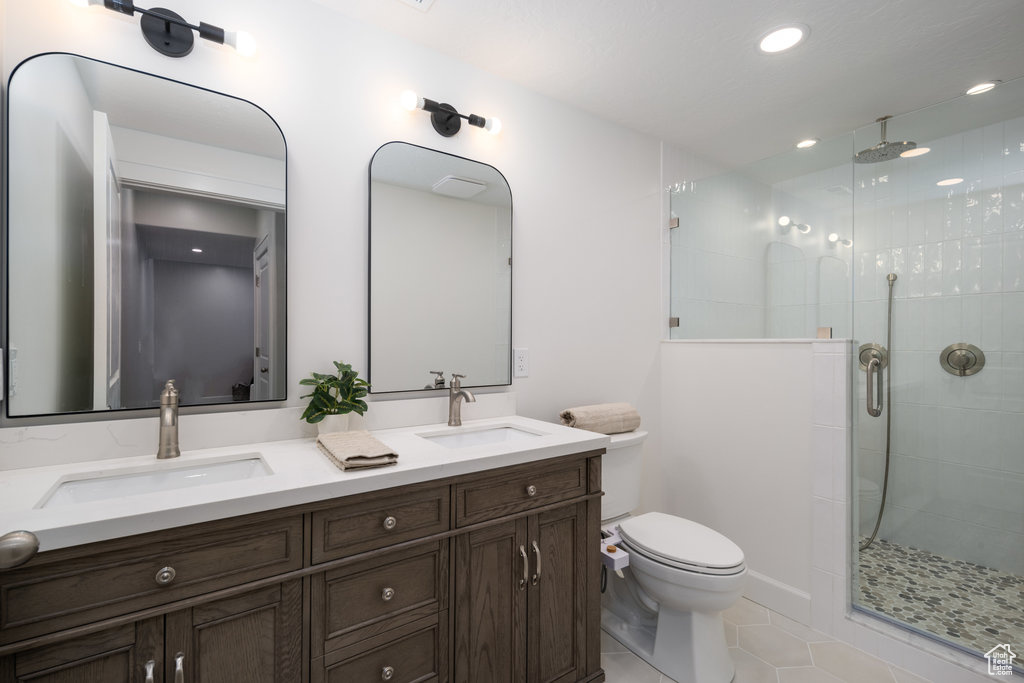 Bathroom with vanity with extensive cabinet space, double sink, a shower with shower door, tile flooring, and toilet