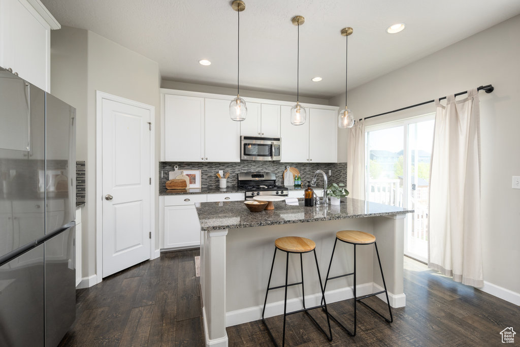 Kitchen with backsplash, stainless steel appliances, dark wood-type flooring, white cabinetry, and pendant lighting
