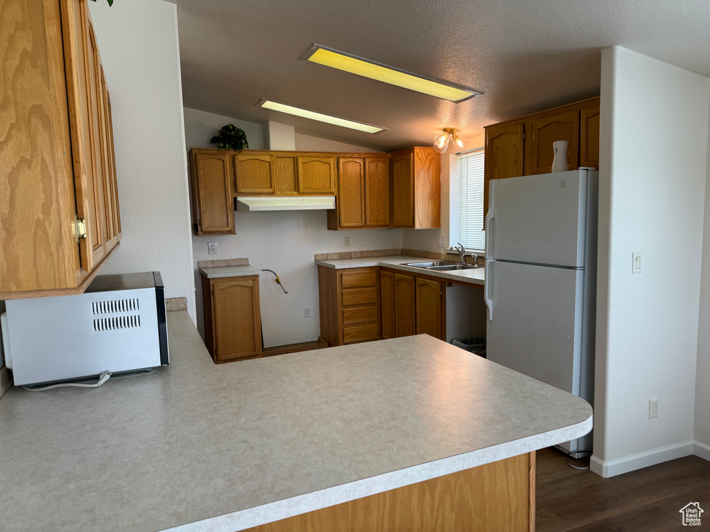 Kitchen featuring kitchen peninsula, dark hardwood / wood-style floors, a textured ceiling, sink, and white refrigerator