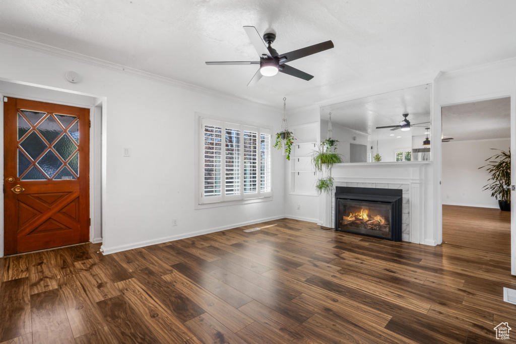 Unfurnished living room with dark hardwood / wood-style flooring, ceiling fan, crown molding, and a tiled fireplace