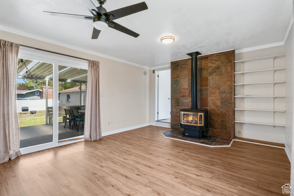 Unfurnished living room featuring ornamental molding, a wood stove, wood-type flooring, and ceiling fan