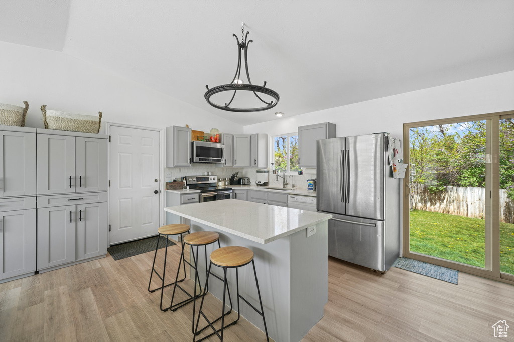 Kitchen featuring decorative light fixtures, stainless steel appliances, vaulted ceiling, a kitchen island, and light hardwood / wood-style floors