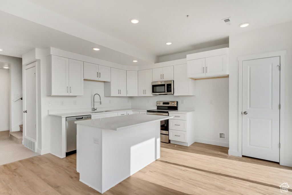 Kitchen with appliances with stainless steel finishes, a center island, white cabinets, sink, and light hardwood / wood-style floors