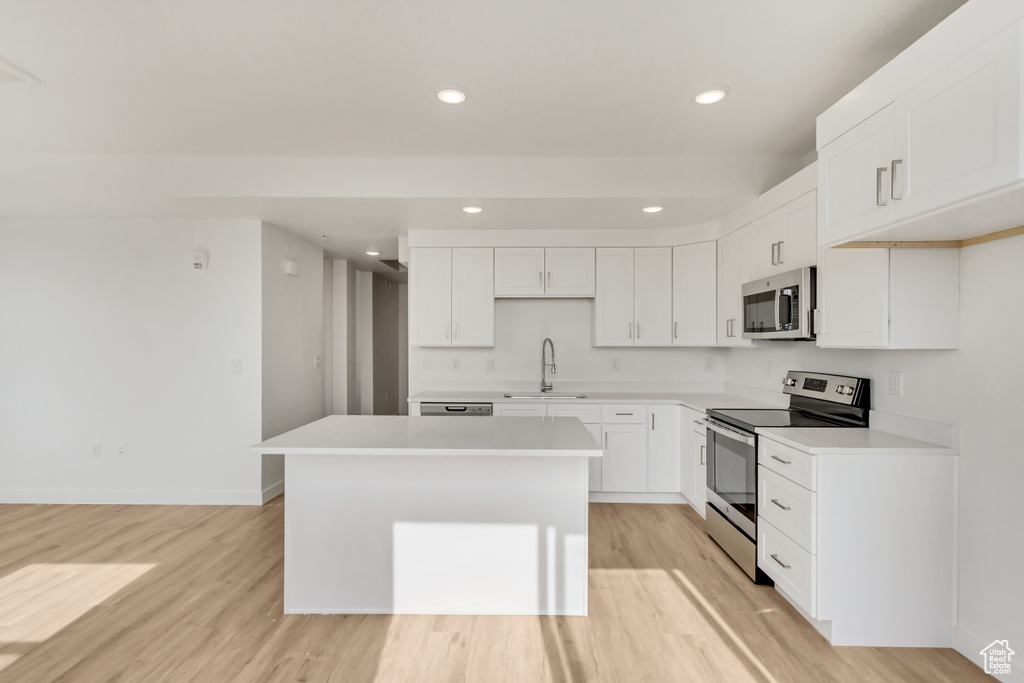 Kitchen with appliances with stainless steel finishes, white cabinets, sink, a center island, and light wood-type flooring