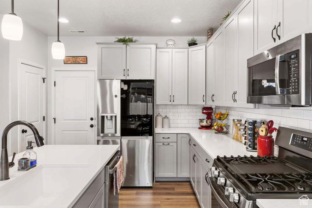 Kitchen featuring appliances with stainless steel finishes, light hardwood / wood-style flooring, tasteful backsplash, sink, and pendant lighting