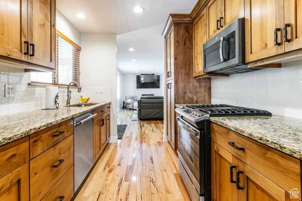 Kitchen featuring tasteful backsplash, stainless steel appliances, light stone counters, and light wood-type flooring
