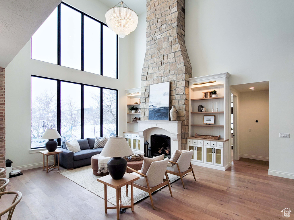 Living room featuring a chandelier, a large fireplace, a high ceiling, and light wood-type flooring