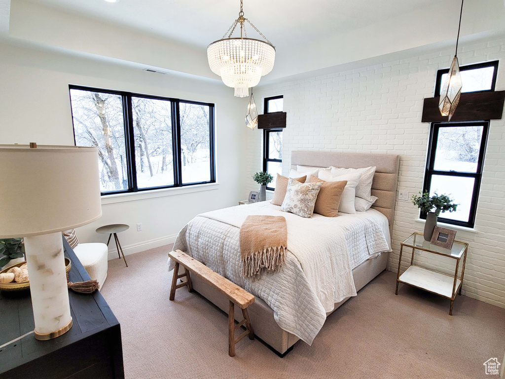 Carpeted bedroom featuring brick wall and an inviting chandelier