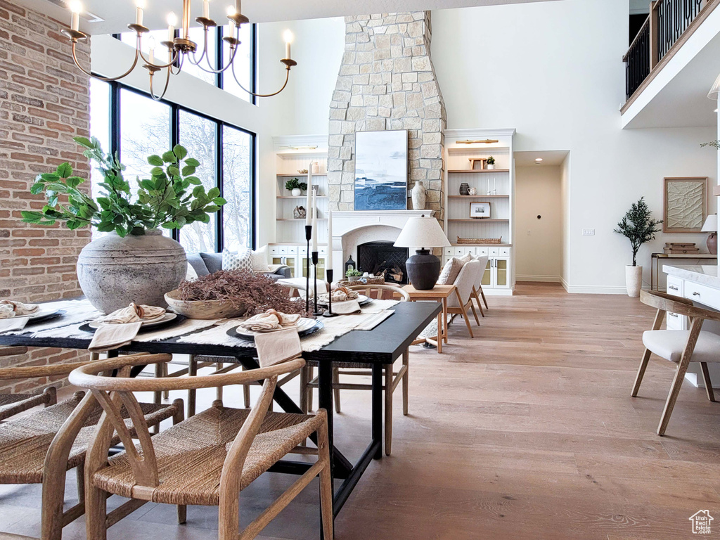 Dining space featuring a large fireplace, a notable chandelier, a towering ceiling, and light hardwood / wood-style floors