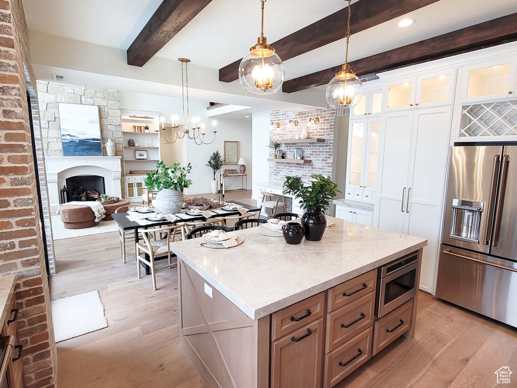 Kitchen featuring hanging light fixtures, appliances with stainless steel finishes, white cabinetry, light wood-type flooring, and a center island