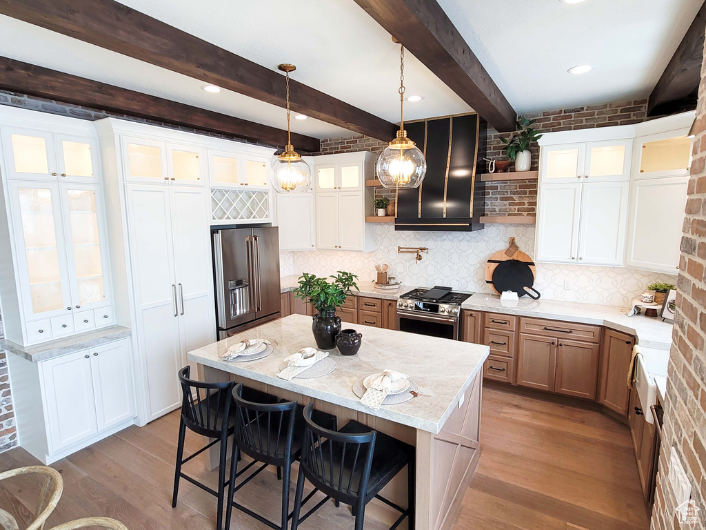 Kitchen with light stone countertops, light wood-type flooring, a large island, beamed ceiling, and high end appliances