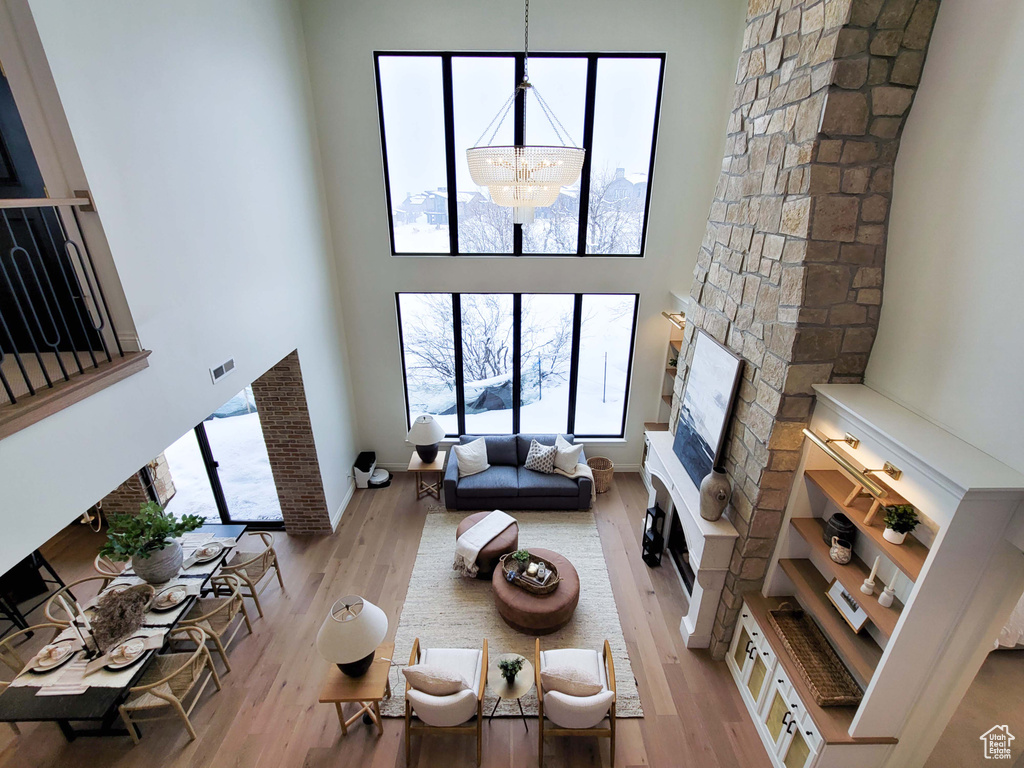 Living room featuring a chandelier, a high ceiling, a stone fireplace, and light hardwood / wood-style floors