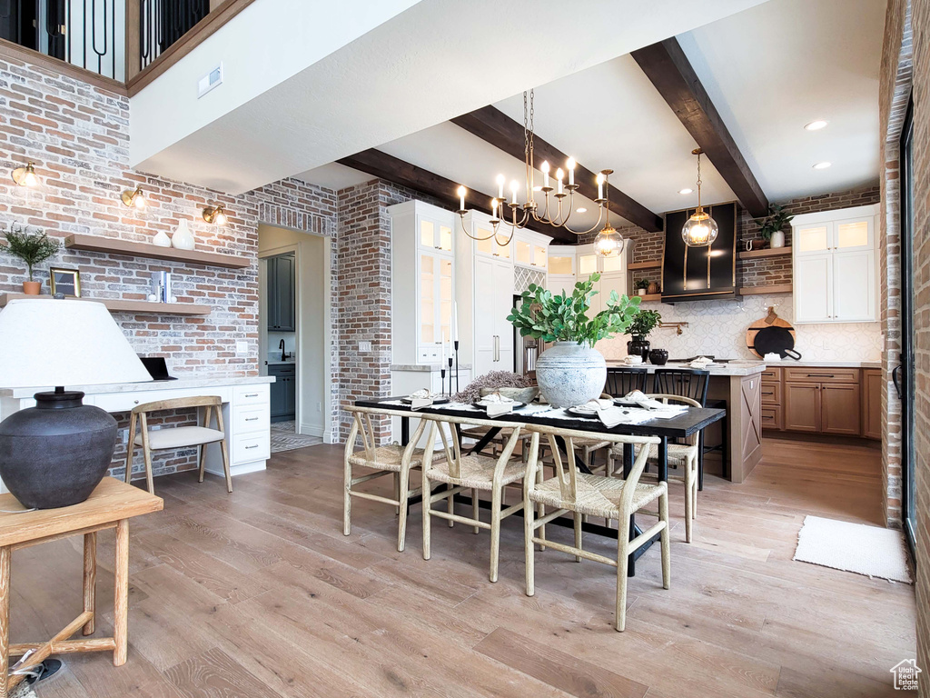 Dining room featuring beamed ceiling, a notable chandelier, light hardwood / wood-style floors, and brick wall