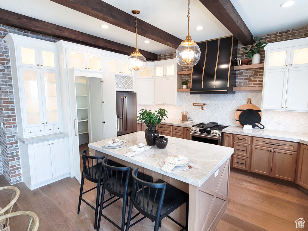 Kitchen featuring beam ceiling, white cabinetry, light stone countertops, light hardwood / wood-style floors, and a center island