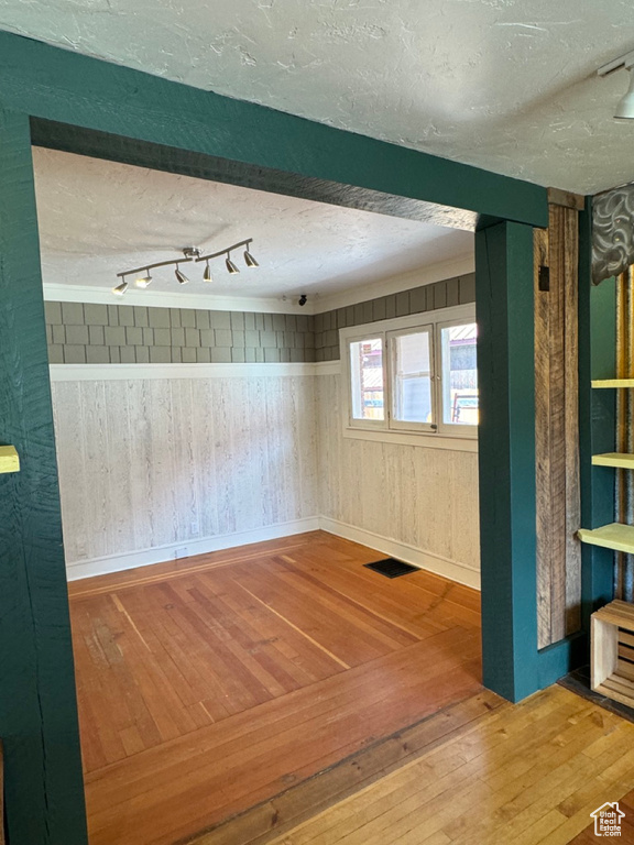 Spare room with wood walls, track lighting, hardwood / wood-style flooring, and a textured ceiling