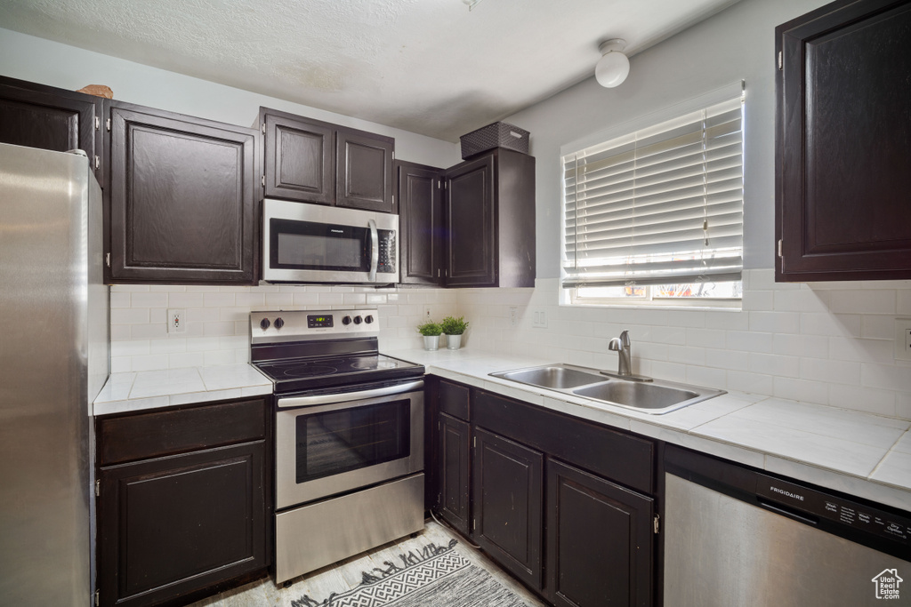 Kitchen featuring dark brown cabinetry, sink, tasteful backsplash, and stainless steel appliances