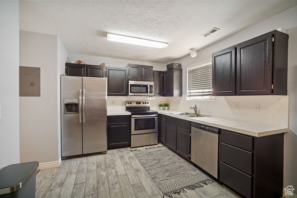 Kitchen featuring dark brown cabinets, backsplash, stainless steel appliances, sink, and light wood-type flooring