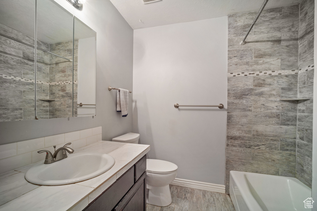 Full bathroom featuring hardwood / wood-style flooring, tiled shower / bath combo, toilet, and vanity