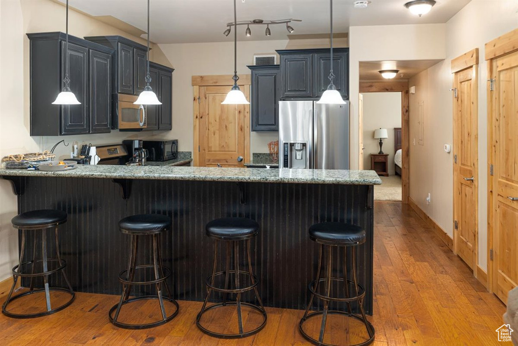 Kitchen with hardwood / wood-style floors, decorative light fixtures, stainless steel appliances, kitchen peninsula, and a kitchen breakfast bar