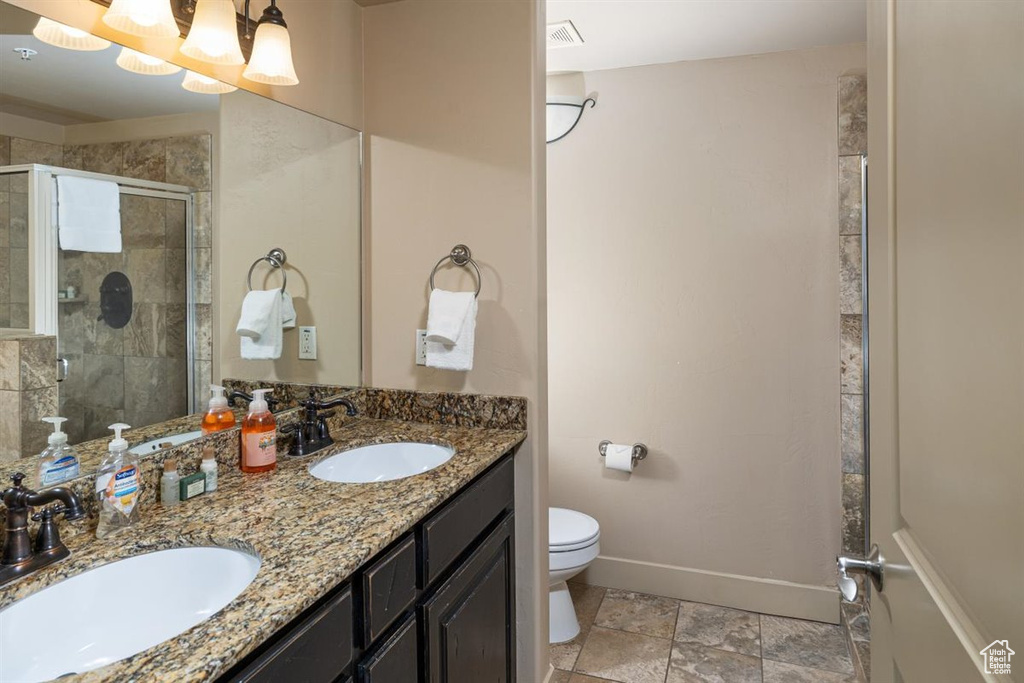 Bathroom featuring tile flooring, dual sinks, oversized vanity, toilet, and a shower with door