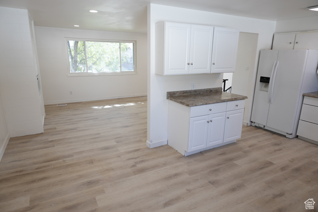 Kitchen with white cabinets, light hardwood / wood-style flooring, and white refrigerator with ice dispenser