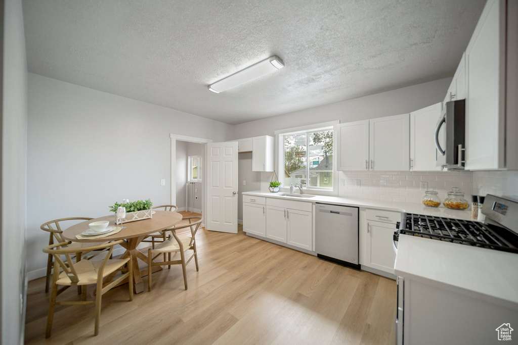 Kitchen featuring backsplash, light hardwood / wood-style flooring, stainless steel appliances, white cabinets, and sink