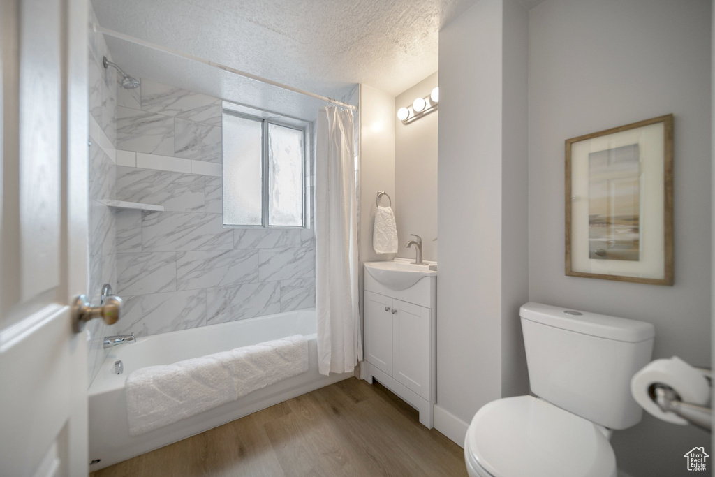 Full bathroom with shower / bath combination with curtain, vanity, hardwood / wood-style floors, toilet, and a textured ceiling