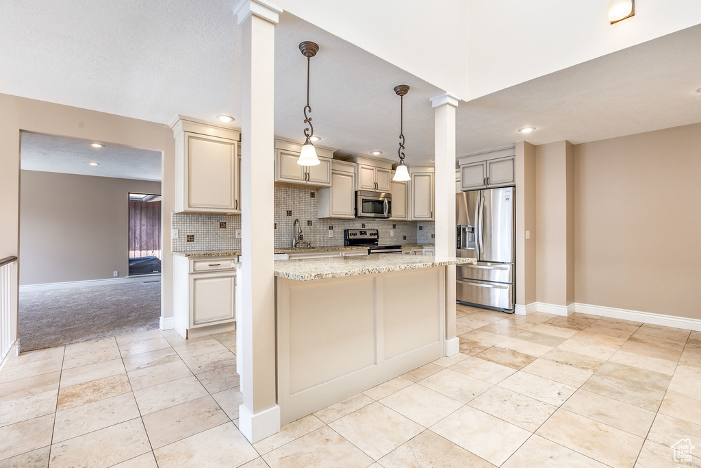 Kitchen featuring decorative light fixtures, light stone countertops, backsplash, appliances with stainless steel finishes, and light colored carpet