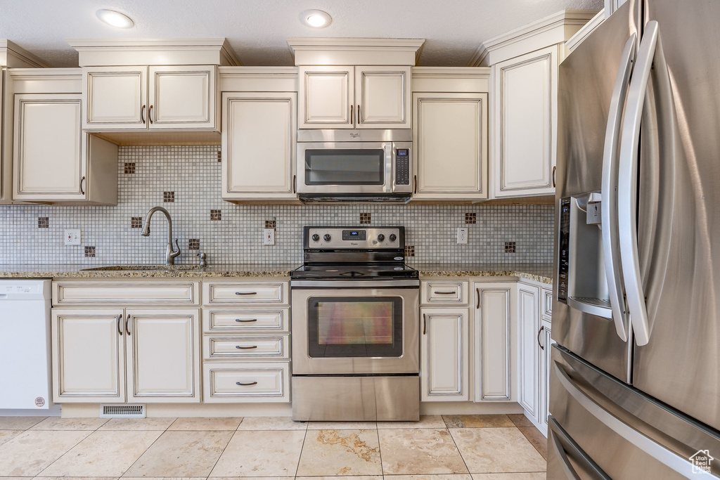 Kitchen with appliances with stainless steel finishes, light tile floors, sink, backsplash, and light stone countertops