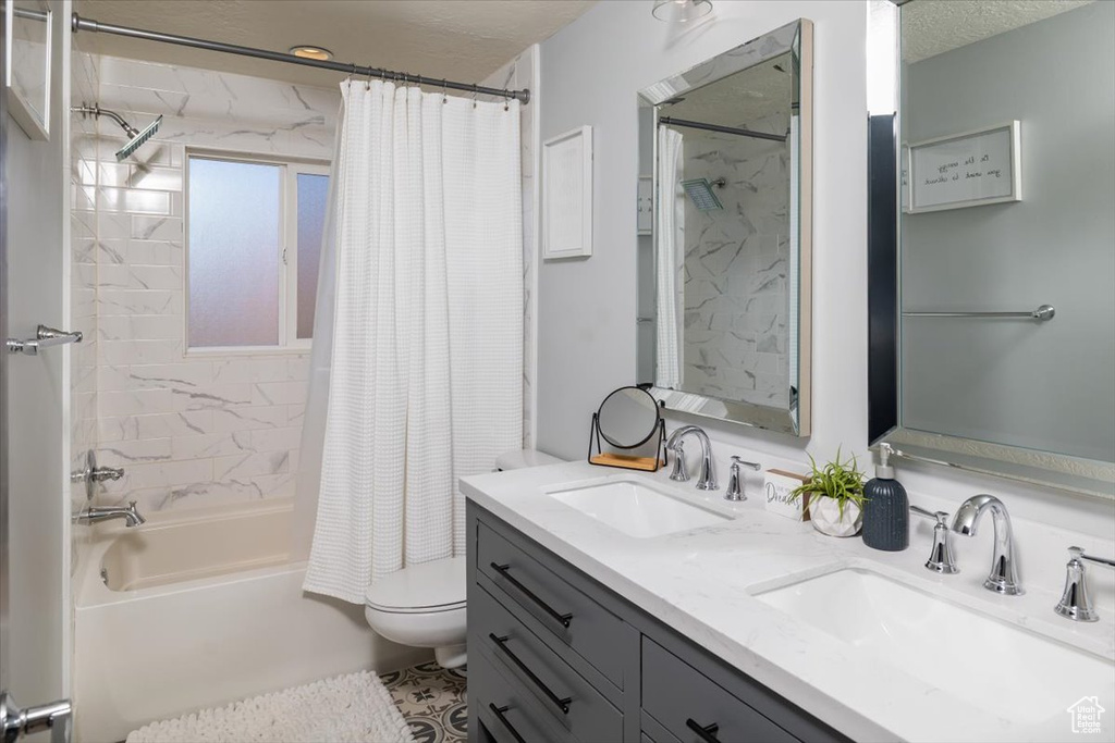 Full bathroom featuring shower / bath combo, oversized vanity, dual sinks, toilet, and a textured ceiling