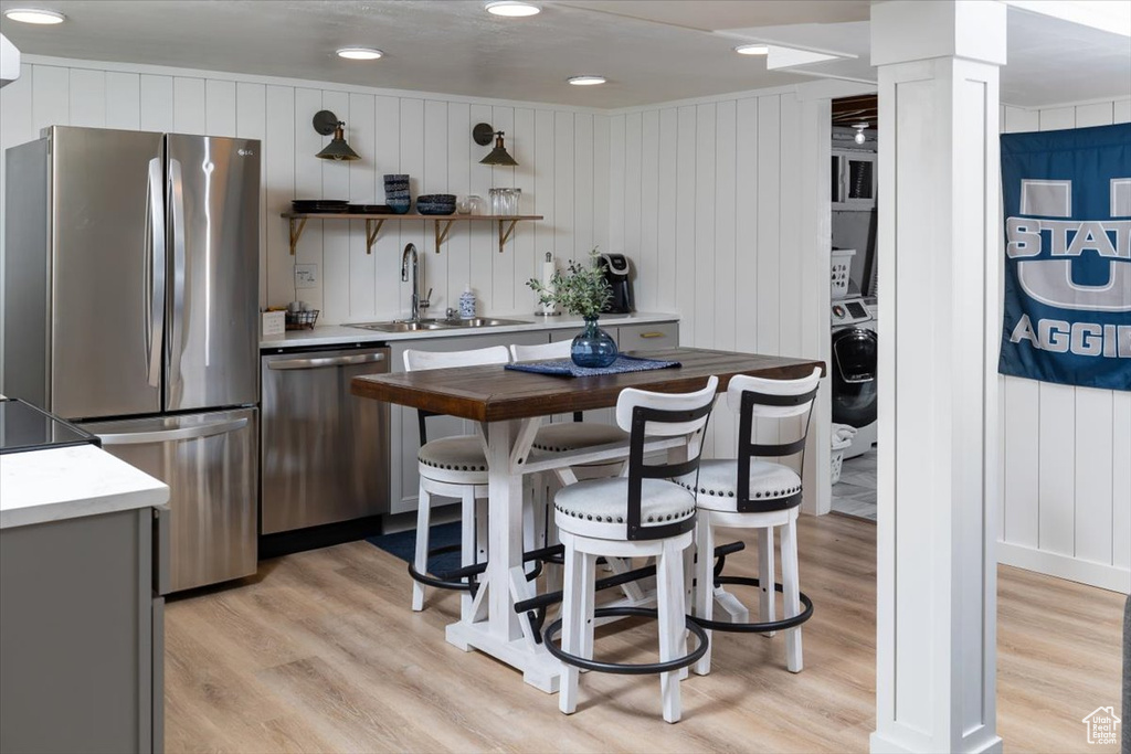 Kitchen featuring appliances with stainless steel finishes, decorative columns, sink, and light wood-type flooring