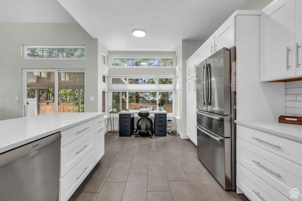 Kitchen featuring tasteful backsplash, stainless steel appliances, light tile flooring, and white cabinetry