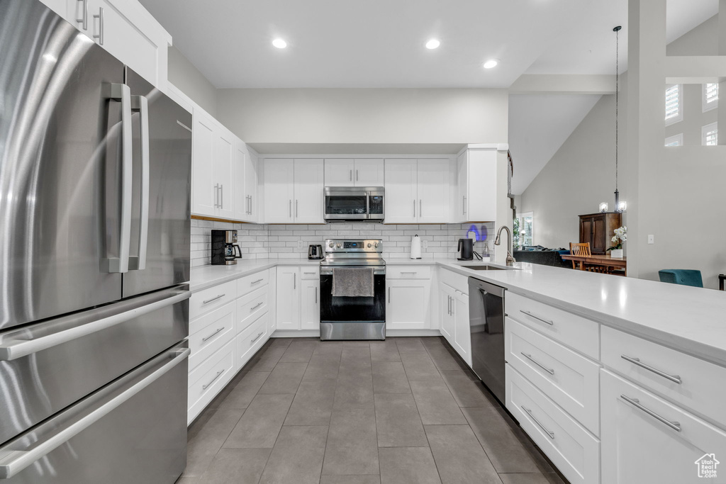 Kitchen with tile flooring, appliances with stainless steel finishes, white cabinets, sink, and tasteful backsplash
