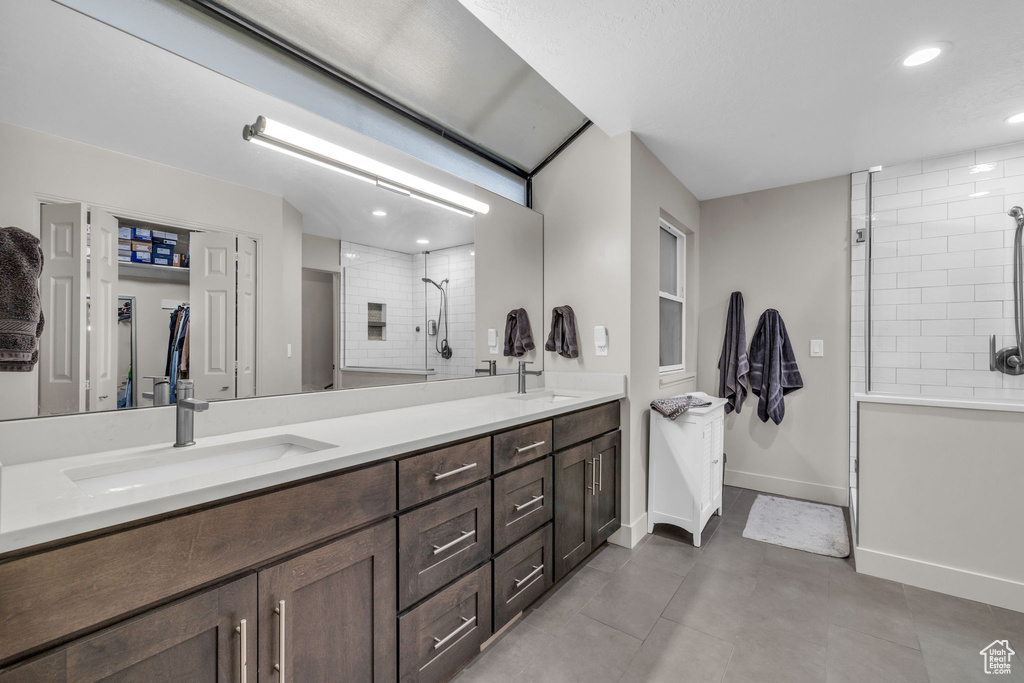 Bathroom featuring vanity with extensive cabinet space, double sink, tile floors, and a tile shower