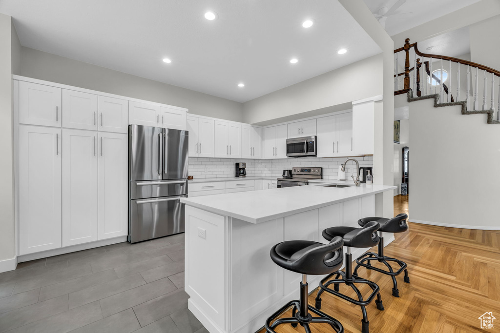 Kitchen featuring appliances with stainless steel finishes, sink, white cabinetry, kitchen peninsula, and light parquet floors