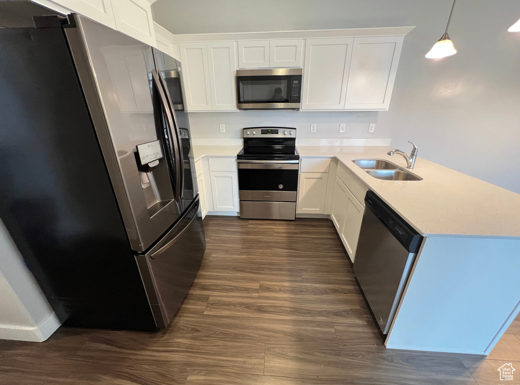 Kitchen with white cabinets, dark wood-type flooring, kitchen peninsula, appliances with stainless steel finishes, and sink