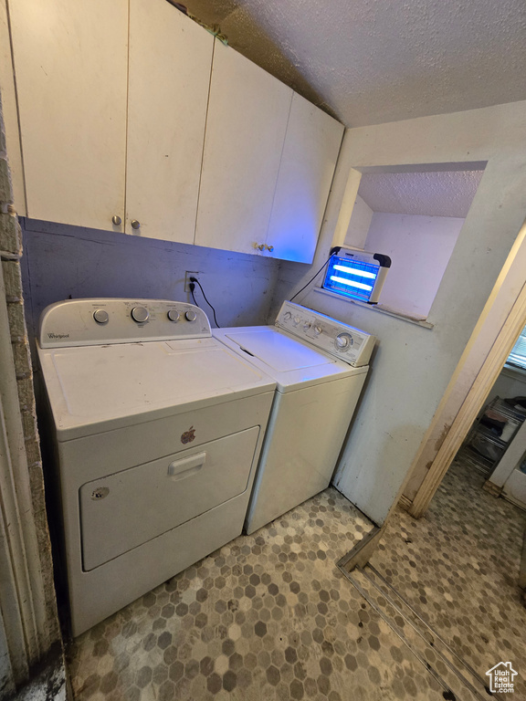Clothes washing area featuring a textured ceiling, cabinets, light tile floors, and washer and clothes dryer