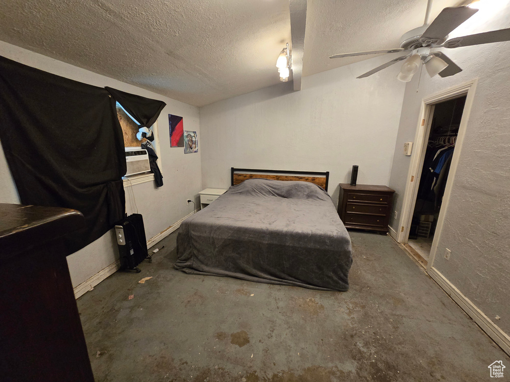 Bedroom featuring a walk in closet, ceiling fan, concrete floors, and a textured ceiling