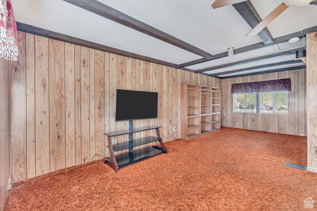 Unfurnished living room with carpet flooring, wood walls, and beamed ceiling