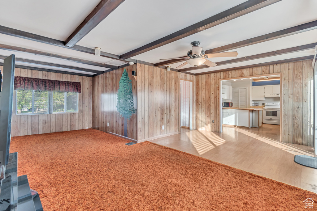 Empty room featuring light colored carpet, beam ceiling, ceiling fan, and wooden walls