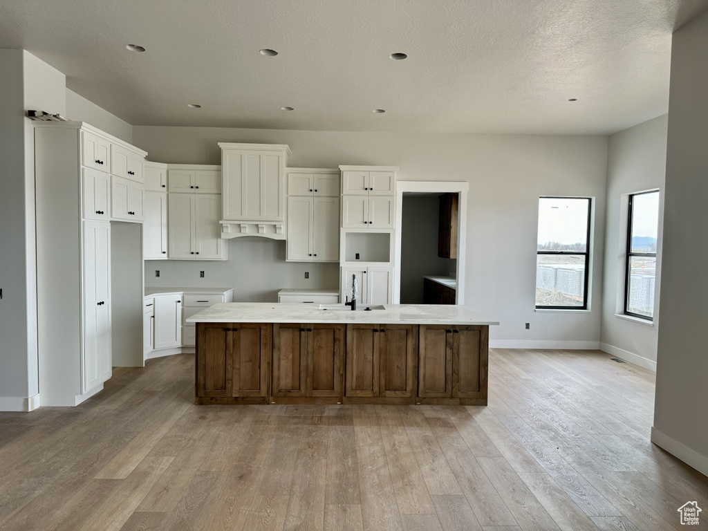Kitchen featuring light hardwood / wood-style flooring, sink, an island with sink, and white cabinetry
