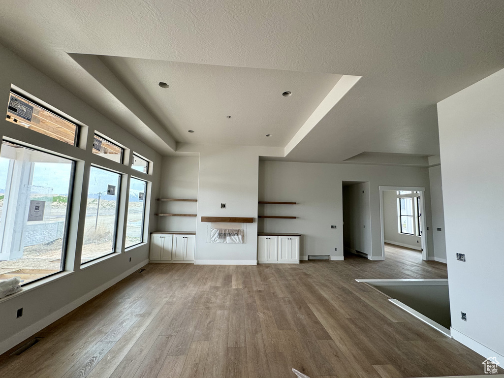 Unfurnished living room with a textured ceiling, hardwood / wood-style floors, and a tray ceiling