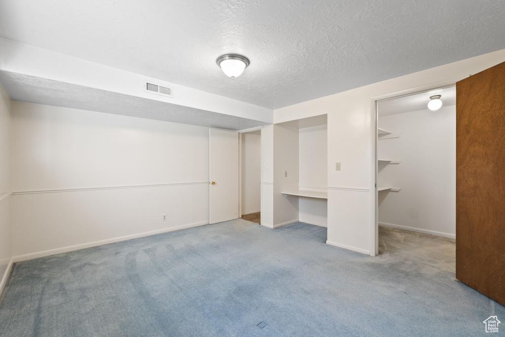 Unfurnished bedroom with a closet, a textured ceiling, carpet floors, and a walk in closet